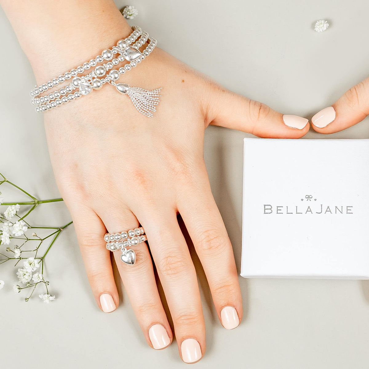 Hand wearing silver stacking bracelets and stacking rings with charms, with a 'Bella Jane' box in the background