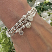 Silver beaded stacking bracelets with charms on a wrist against a floral background