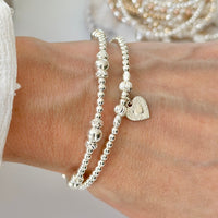 Silver beaded bracelet duo with a delicate heart charm on a wrist against a neutral background