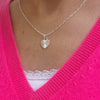 Silver necklace with a heart shape pendant, featuring the angel number 1111, worn by a lady wearing a bright pink v-neck sweater.
