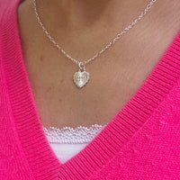 Silver necklace with a heart shape pendant, featuring the angel number 1111, worn by a lady wearing a bright pink v-neck sweater.