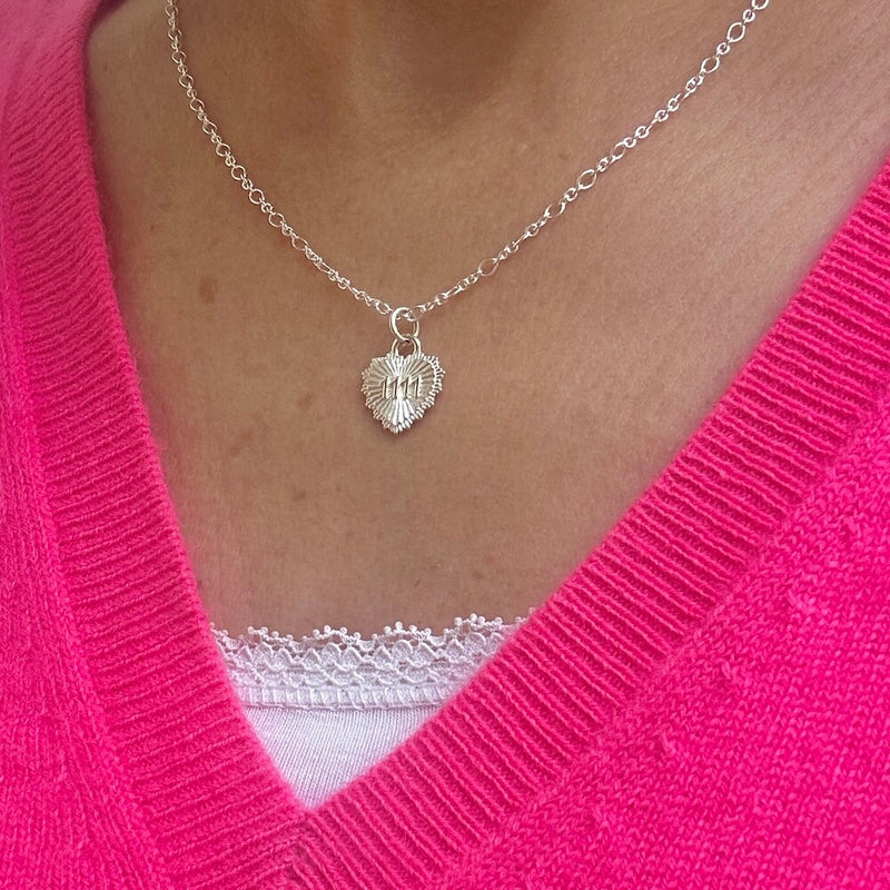 Silver necklace with a heart shape pendant, featuring the angel number 1111, worn by a lady wearing a bright pink v-neck sweater.