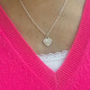 Necklace with a heart-shaped pendant featuring angel number 222, worn by a lady wearing a bright pink v-neck sweater.