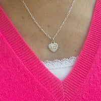 Necklace with a heart-shaped pendant featuring angel number 222, worn by a lady wearing a bright pink v-neck sweater.