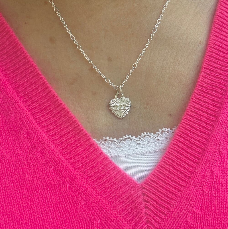 Necklace with a heart-shaped pendant featuring angel number 222, worn by a lady wearing a bright pink v-neck sweater.