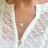 Silver necklace with a heart pendant, featuring the angel number 444, worn by a lady in an off-white textured blouse.