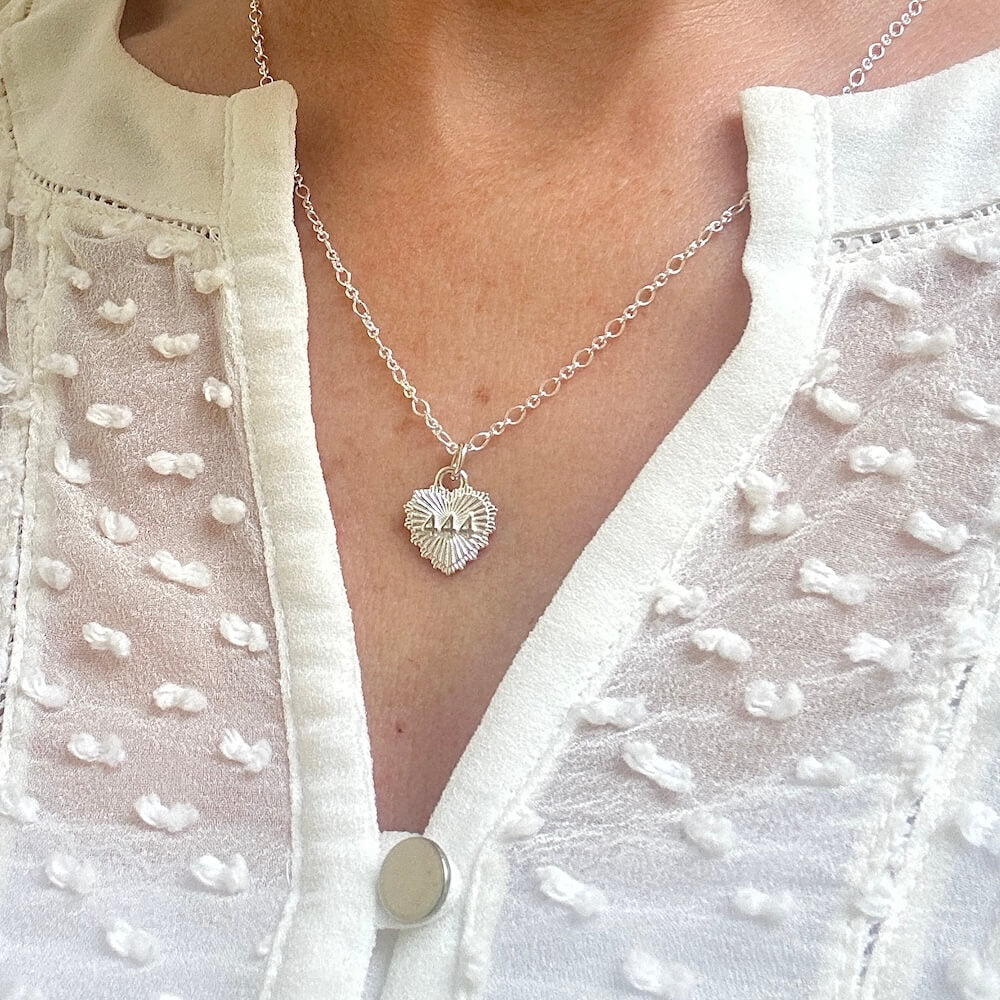 Silver necklace with a heart pendant, featuring the angel number 444, worn by a lady in an off-white textured blouse.