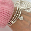 Silver beaded bracelet with heart-shaped charm featuring angel number 555 on the front of the charm, on a white background.