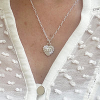 A close up of a model wearing a cream blouse with silver fine chain, featuring a a heart pendant with the angel number 555.