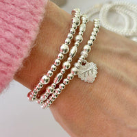 Silver beaded bracelet with heart-shaped charm featuring angel number 777 on the front of the charm, on a white background.