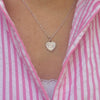 A close up of a a model wearing a silver necklace with a heart pendant featuring angel number 777. The model is wearing a pink and white striped shirt.