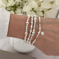 Silver beaded bracelets on a wrist with a blurred floral background, with one bracelet featuring labradorite beads and a sparkly round charm