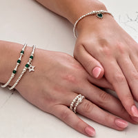 A close up of two hands wearing sterling silver and green onyx stacking bracelets