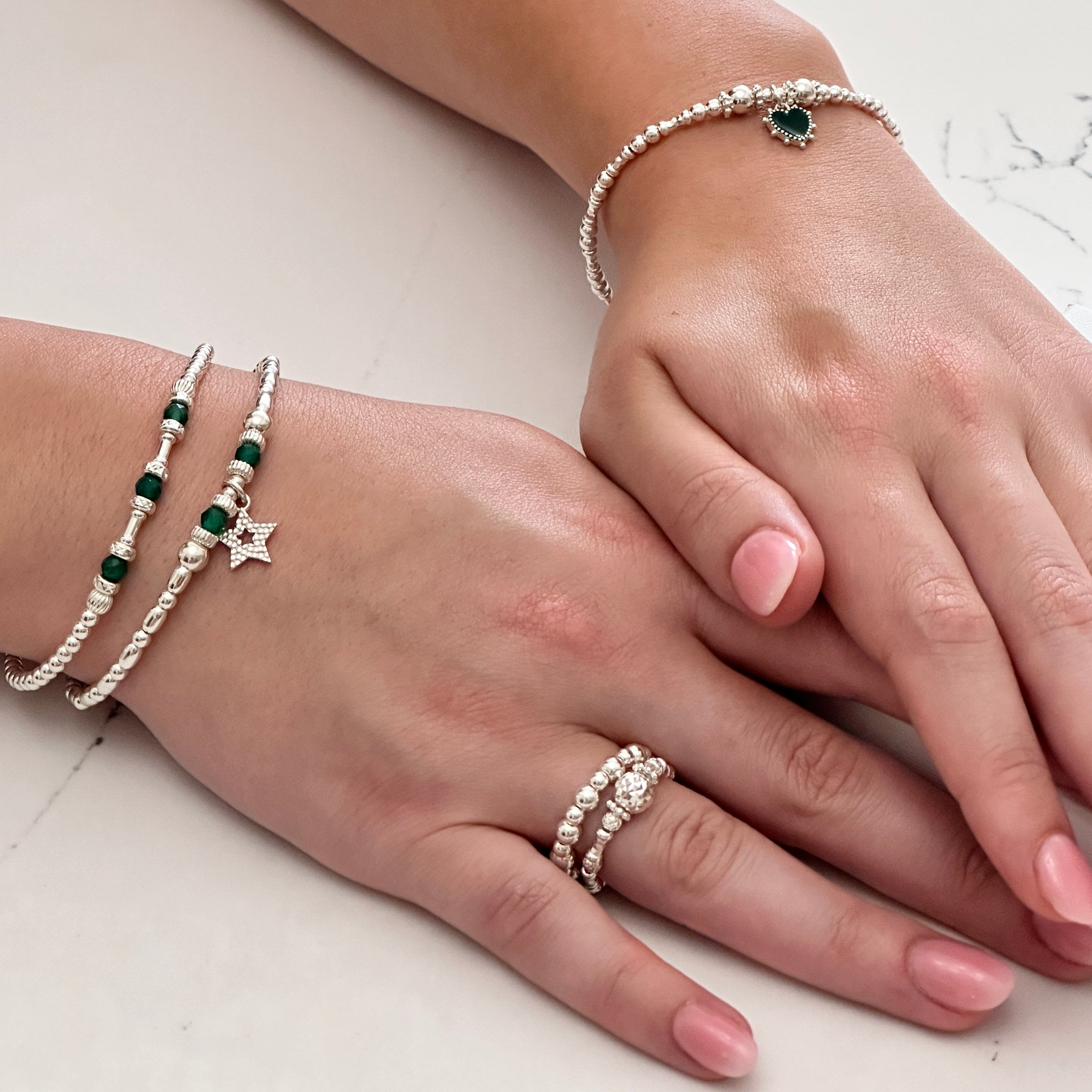 A close up of two hands wearing sterling silver and green onyx stacking bracelets