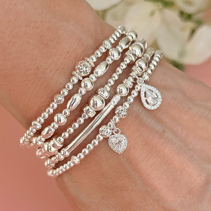 Silver beaded stacking bracelets on a wrist two bracelets featuring sterling silver and cubic zirconia sparkly charms, with a soft background