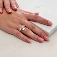 Hand wearing a silver ring with a bow design on a light background
