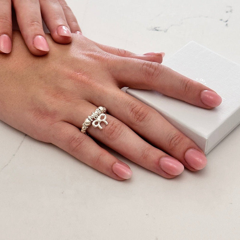 Hand wearing a silver ring with a bow design on a light background