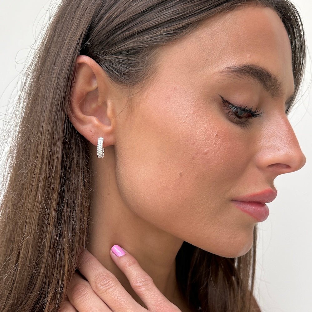 Close-up of a woman wearing a silver hoop earring with a plain background