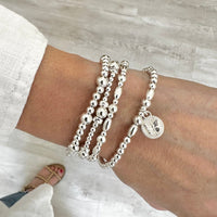 Silver beaded bracelets on a wrist with a neutral background