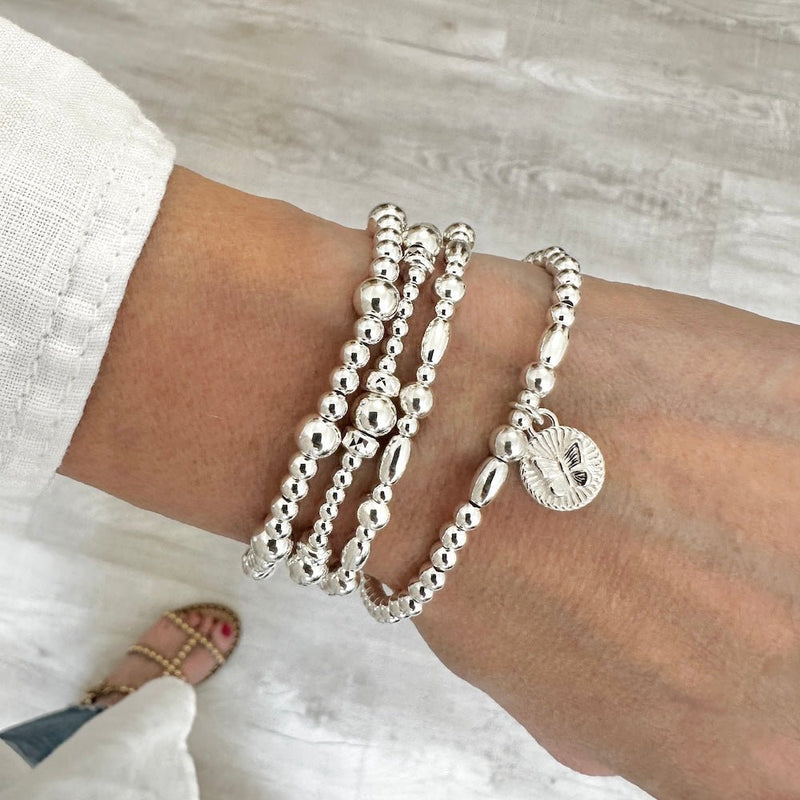 Silver beaded bracelets on a wrist with a neutral background