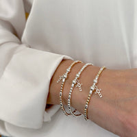 Close-up of a wrist wearing 3 beaded stacking bracelets with cross charms, against a neutral cream shirt background