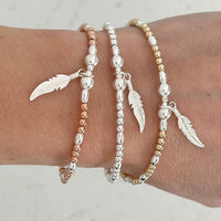 Three beaded bracelets with feather charms on a wrist against a neutral background