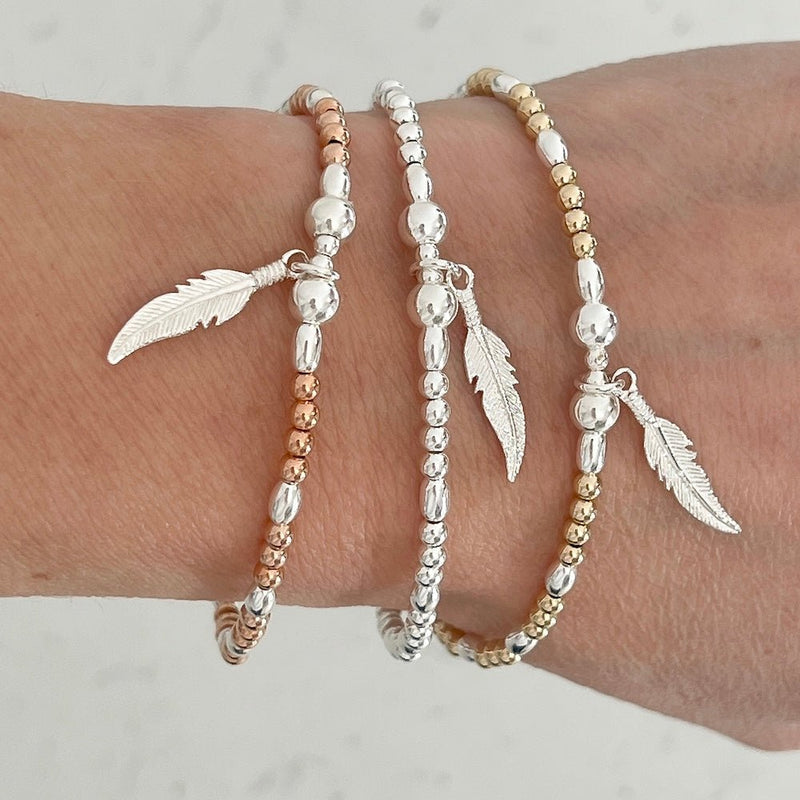 Three beaded bracelets with feather charms on a wrist against a neutral background