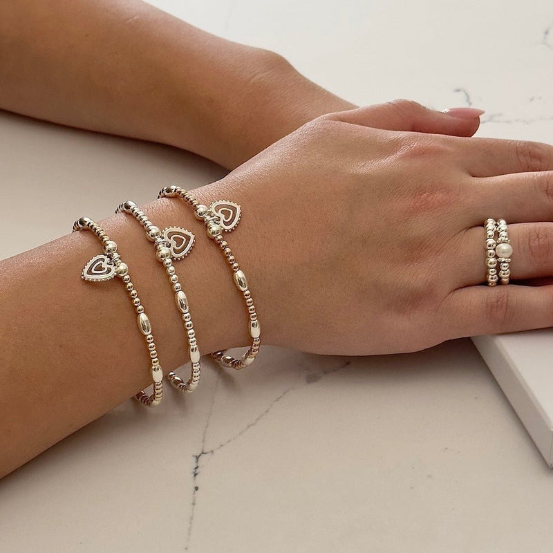 Close-up of a wrist wearing multiple Bella Jane Forever heart stacking bracelets and on a light background