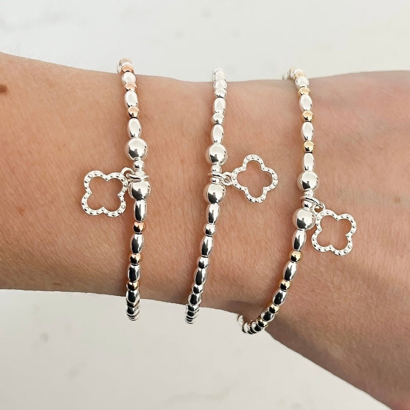 Silver an mixed-metal beaded bracelets with clover charms on a wrist against a white background