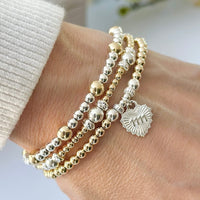 A close up of a woman's wrist wearing a stack of gold and silver beaded stacking bracelets with one bracelet featuring a heart charm with the angel number 1111