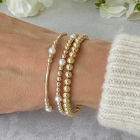 Gold and pearl beaded bracelets on a wrist with a neutral background