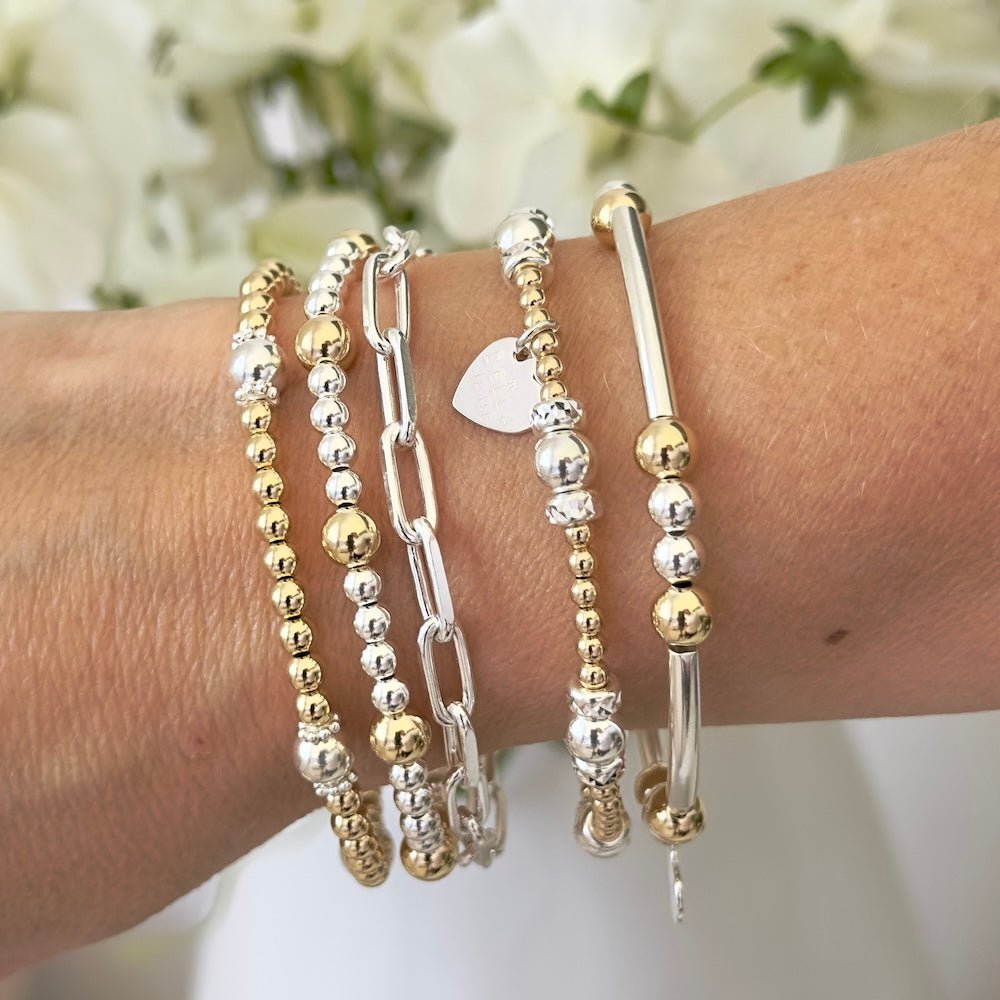 Wrist wearing multiple gold and silver bracelets with a blurred floral background