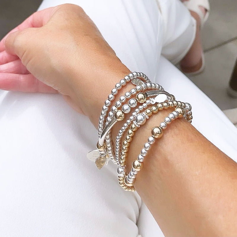 Stack of silver and gold beaded bracelets on a wrist against a white background