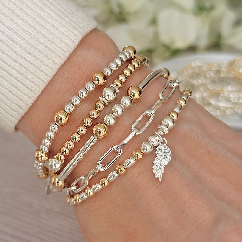 Stack of gold, silver, beaded and chain-link bracelets on a wrist with a blurred floral background