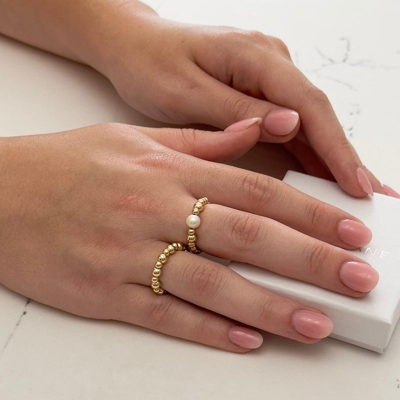 Close-up of hands wearing gold stacking rings with a white background