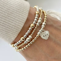 A close-up photo on a white background, of a gold-filled beaded bracelet with sterling silver focal beads and silver heart-shaped charm, featuring angel number 444 on the front of the charm.