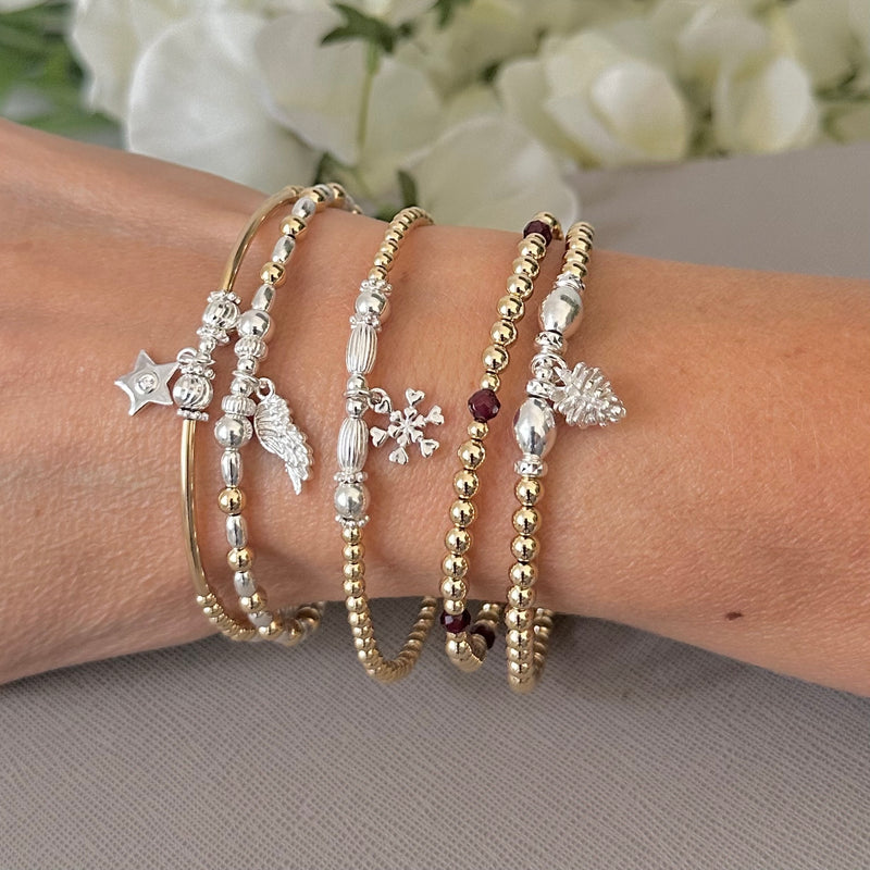 Close up shot of a lady's wrist wearing a stack of Bella Jane gold stacking bracelets, one featuring deep red garnet beads.
