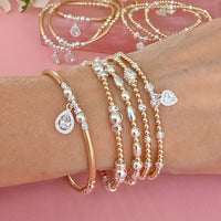 Gold and silver mixed metal beaded stacking bracelets, featuring sterling silver cubic zirconia sparkly charms, on a wrist with a pink background