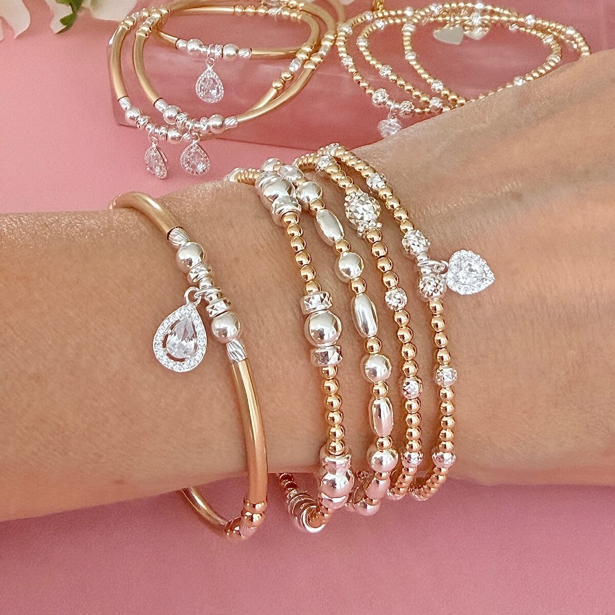 Gold and silver mixed metal beaded stacking bracelets, featuring sterling silver cubic zirconia sparkly charms, on a wrist with a pink background
