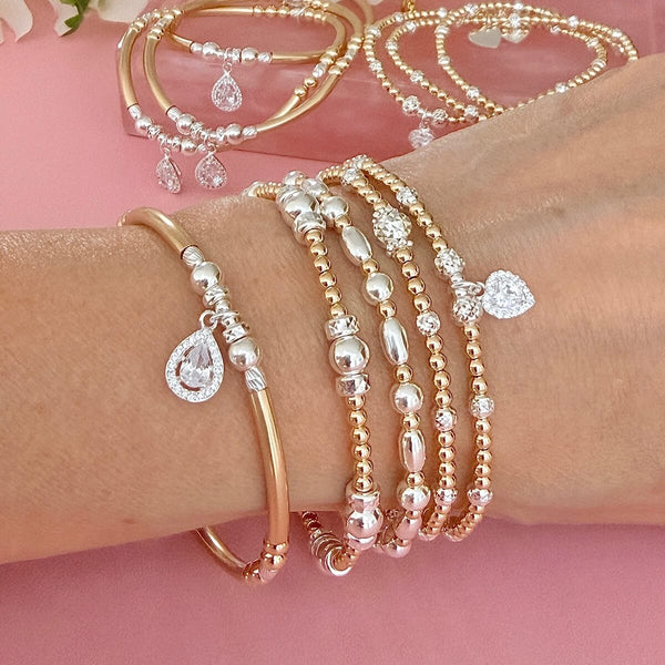 Gold and silver mixed metal beaded stacking bracelets, featuring sterling silver cubic zirconia sparkly charms, on a wrist with a pink background