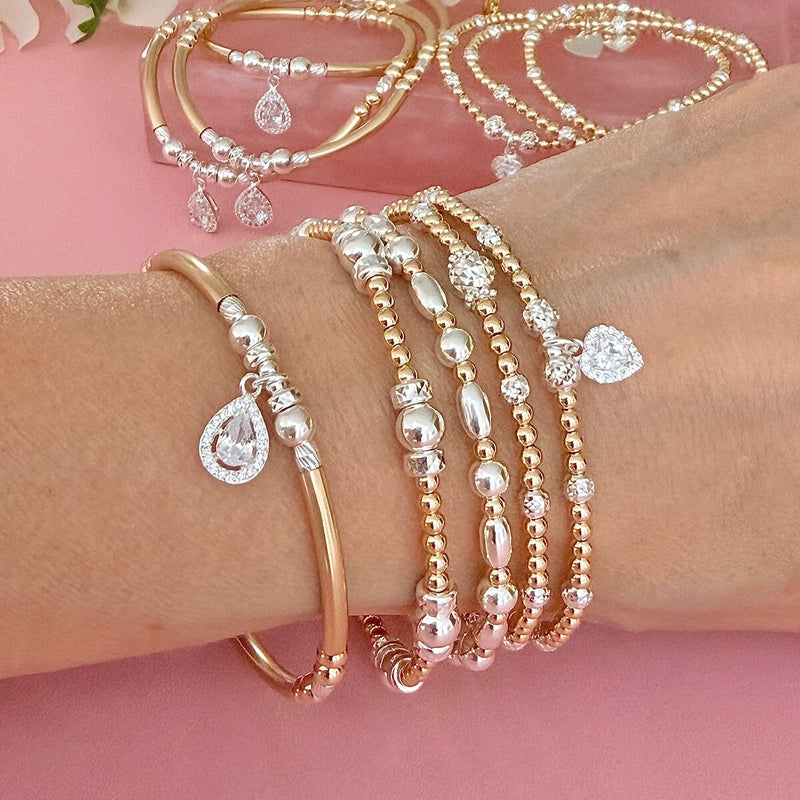 Gold and silver mixed metal beaded stacking bracelets, featuring sterling silver cubic zirconia sparkly charms, on a wrist with a pink background