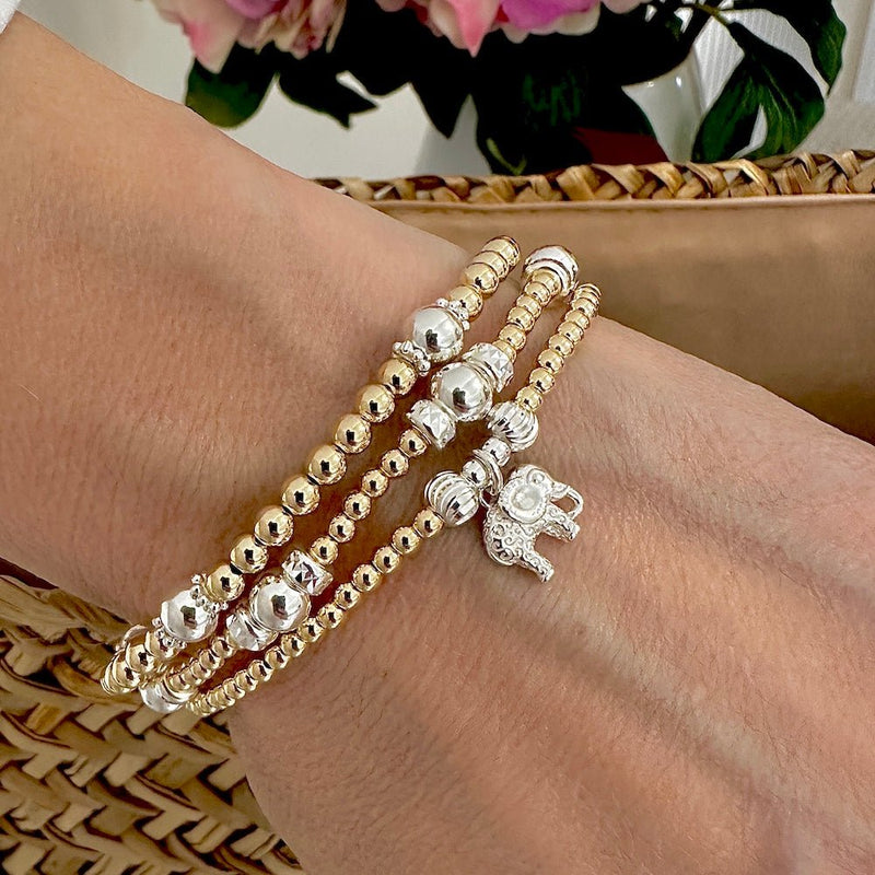 Close-up of a wrist wearing gold and silver beaded bracelets, one with an elephant charm.