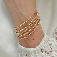 Gold-filled and pink opal beaded stacking bracelet  on a wrist against a white top