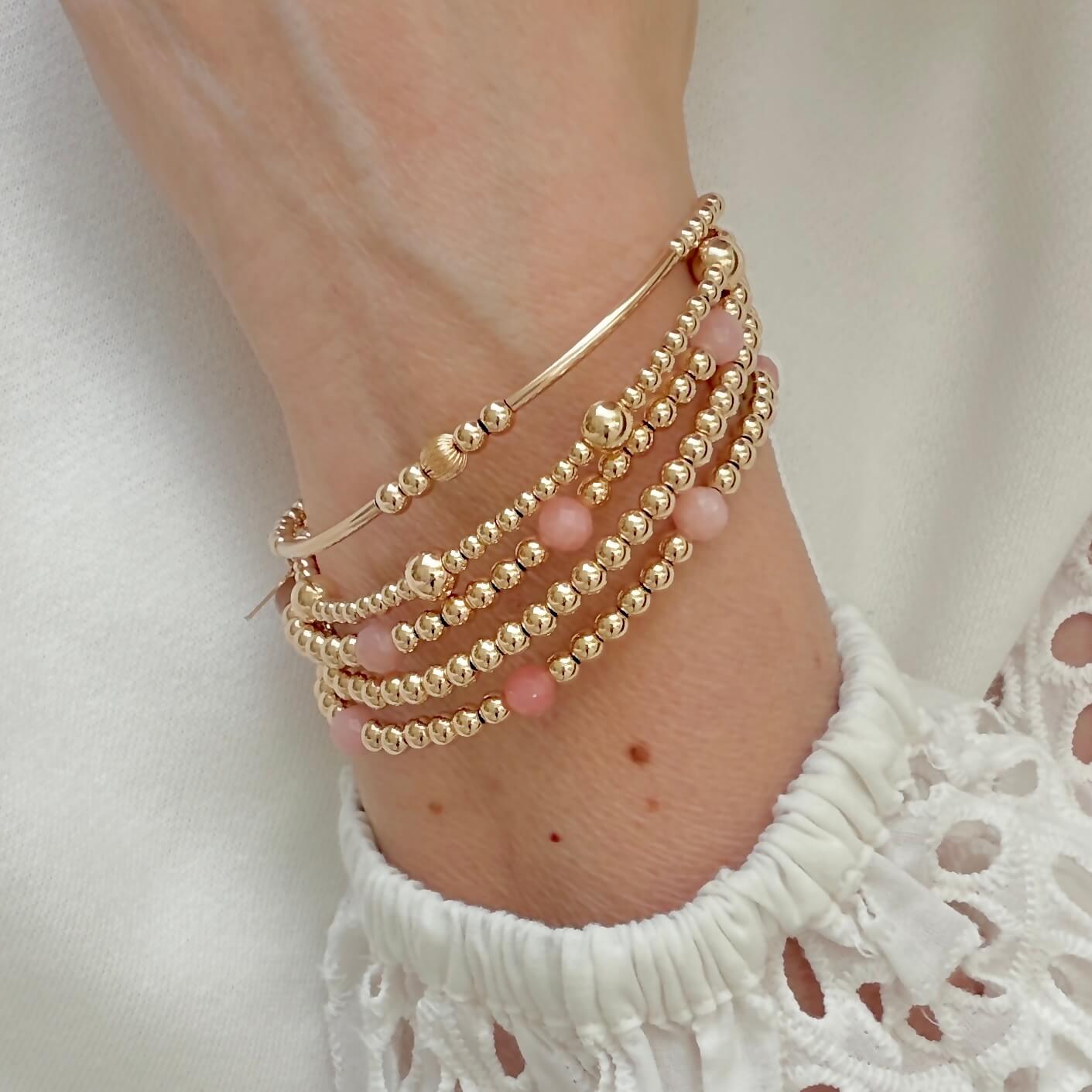 Gold-filled and pink opal beaded stacking bracelet  on a wrist against a white top