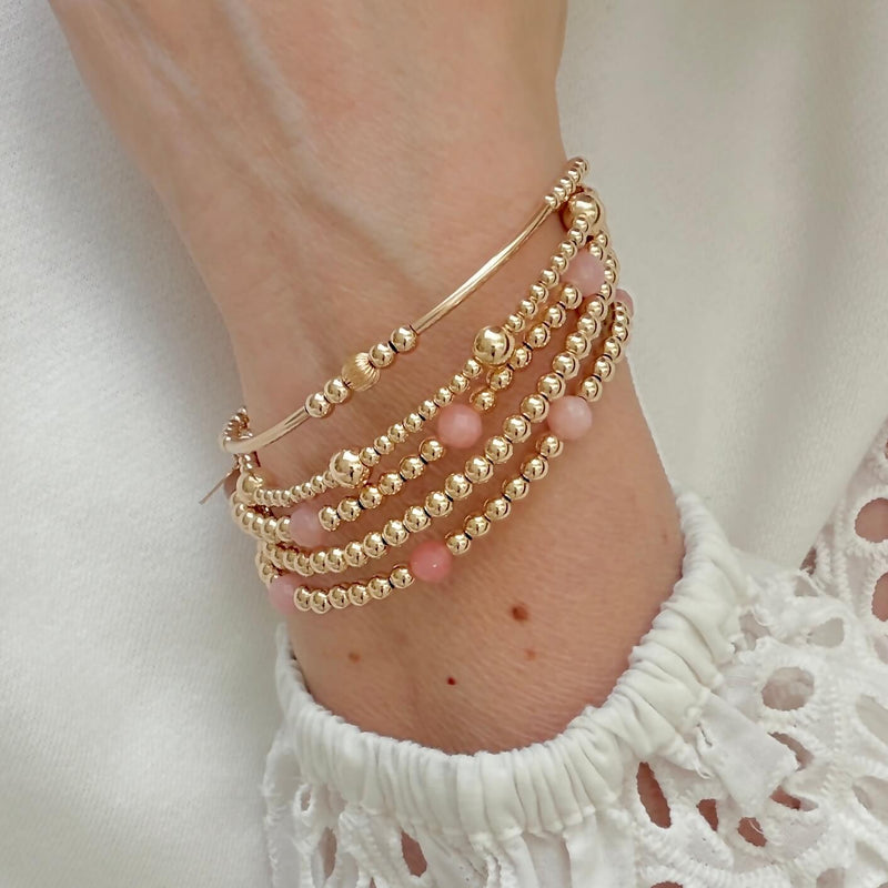 Gold-filled and pink opal beaded stacking bracelet  on a wrist against a white top