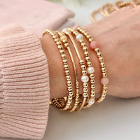 Gold beaded bracelets on a wrist with a soft pink background