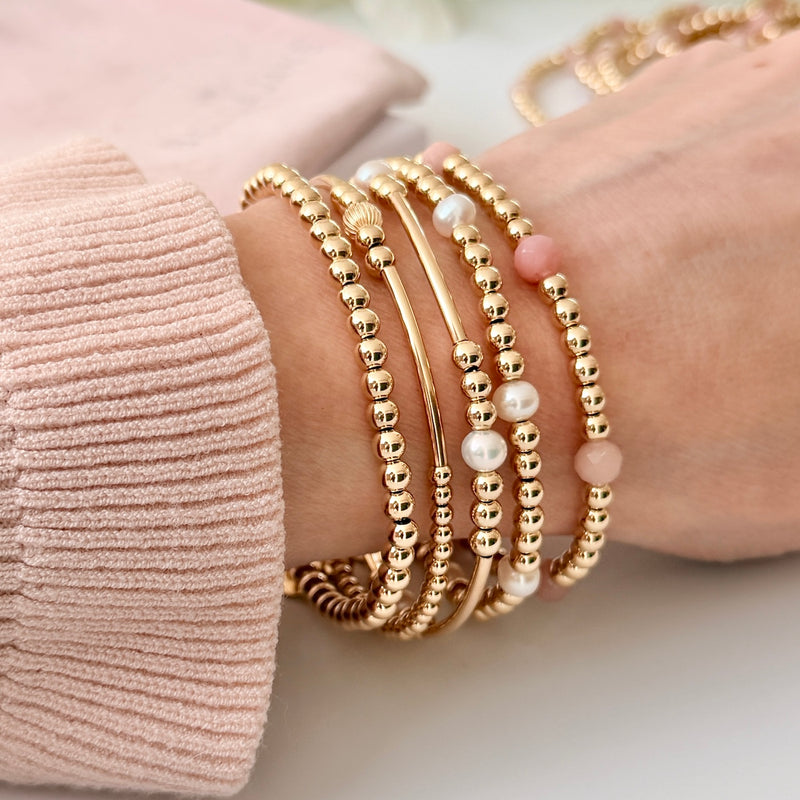 Gold beaded bracelets on a wrist with a soft pink background