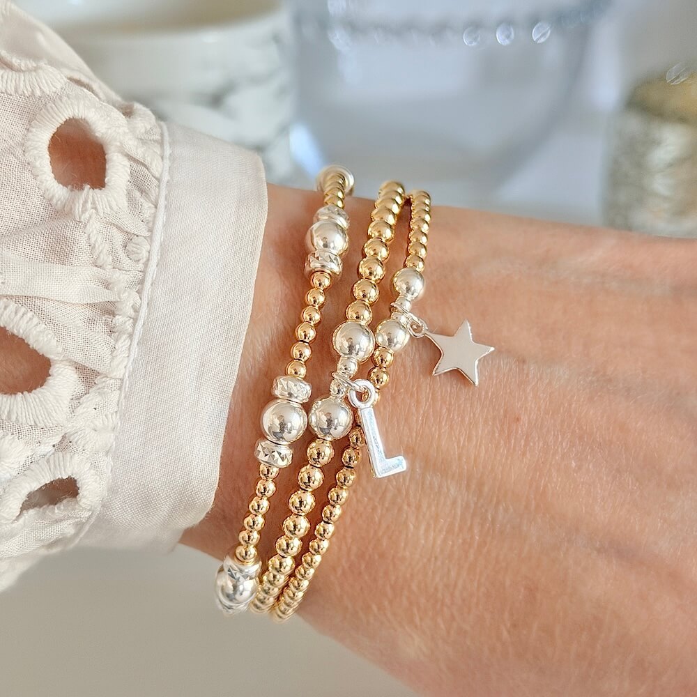 Close-up of a wrist wearing multiple gold and silver beaded stacking bracelets with charms.