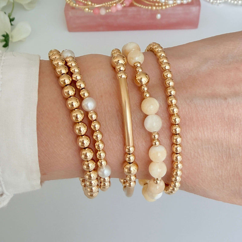 Gold and lemon beaded bracelets on a wrist with a white background
