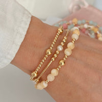 Close-up of a wrist wearing gold and pale lemon beaded bracelets on a neutral background